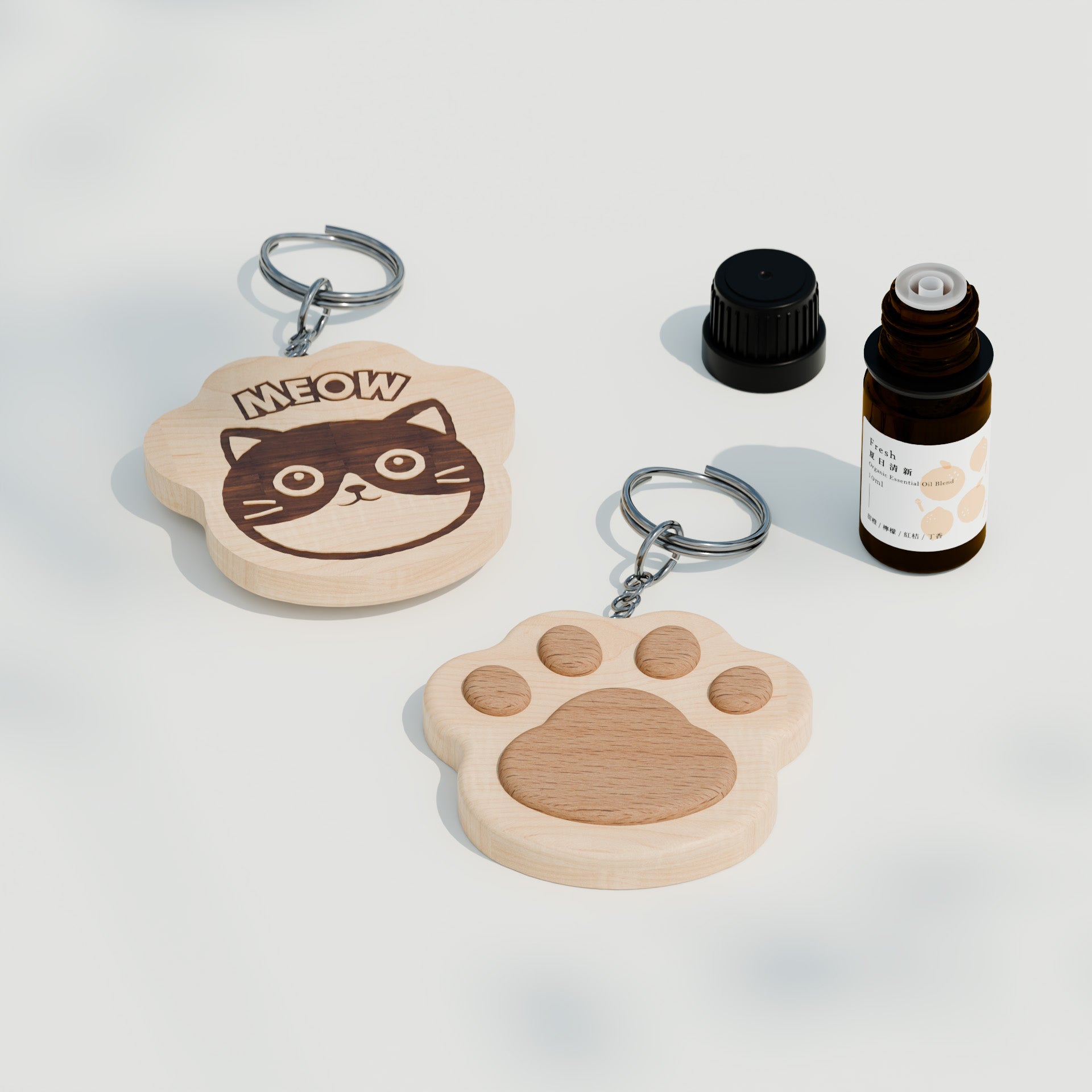 木製貓咪主題鑰匙圈與精油搭配展示圖，畫面中有兩款鑰匙圈，一款為貓咪臉造型，表面鑲嵌深色木紋貓臉並刻有「MEOW」字樣；另一款為貓掌造型，中央嵌有較深色木片。右側可見一瓶精油與黑色瓶蓋，呈現商品可搭配香氛使用的概念。